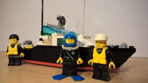 Ein Polizeiboot aus LEGO®, da vor stehen drei Polizisten, zwei mit Schwimmweste, einer mit Taucheranzug.